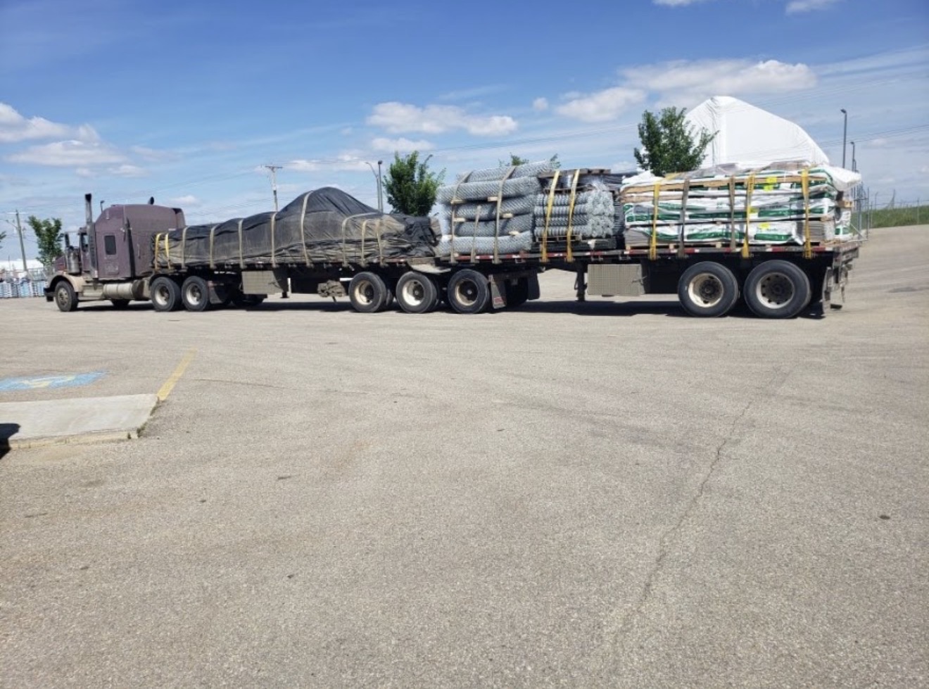 Flatbed loaded with chain-link fencing rolls and pallets of building supplies