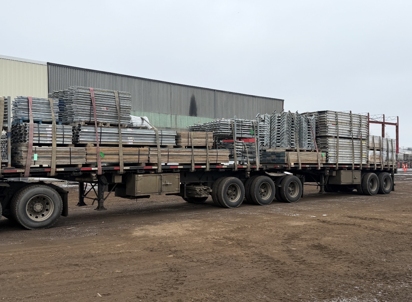 Super B-train flat-deck loaded with scaffolding frames and planks in the yard