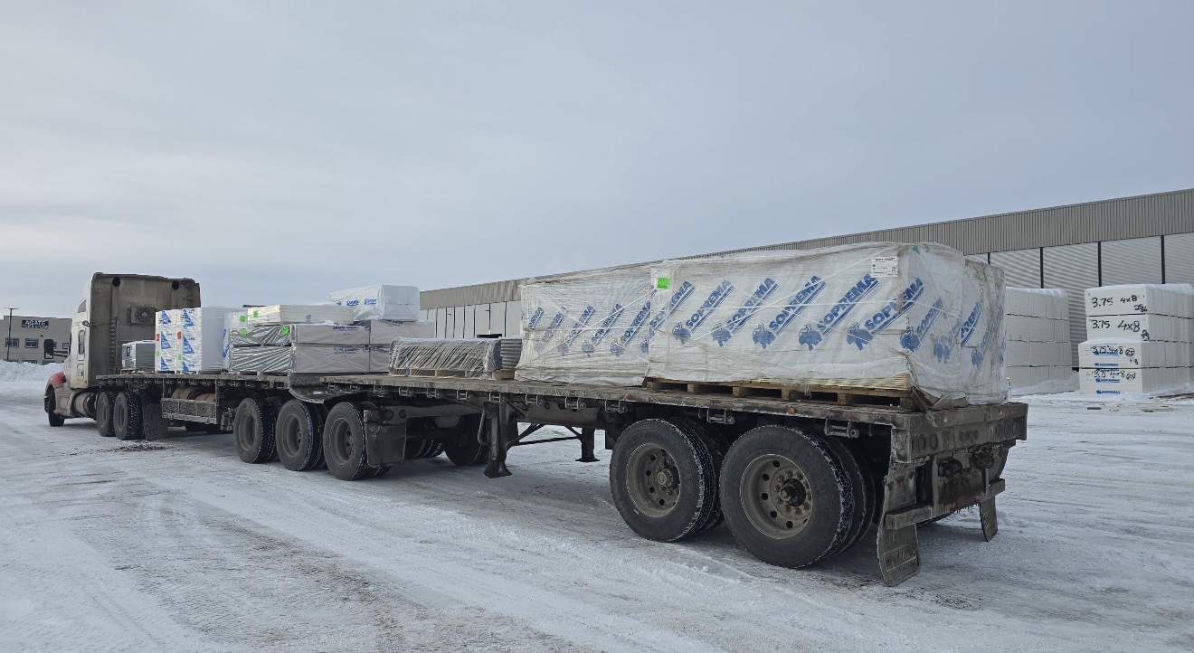 Super B-train flat-deck loaded with palletized Soprema roofing materials in winter