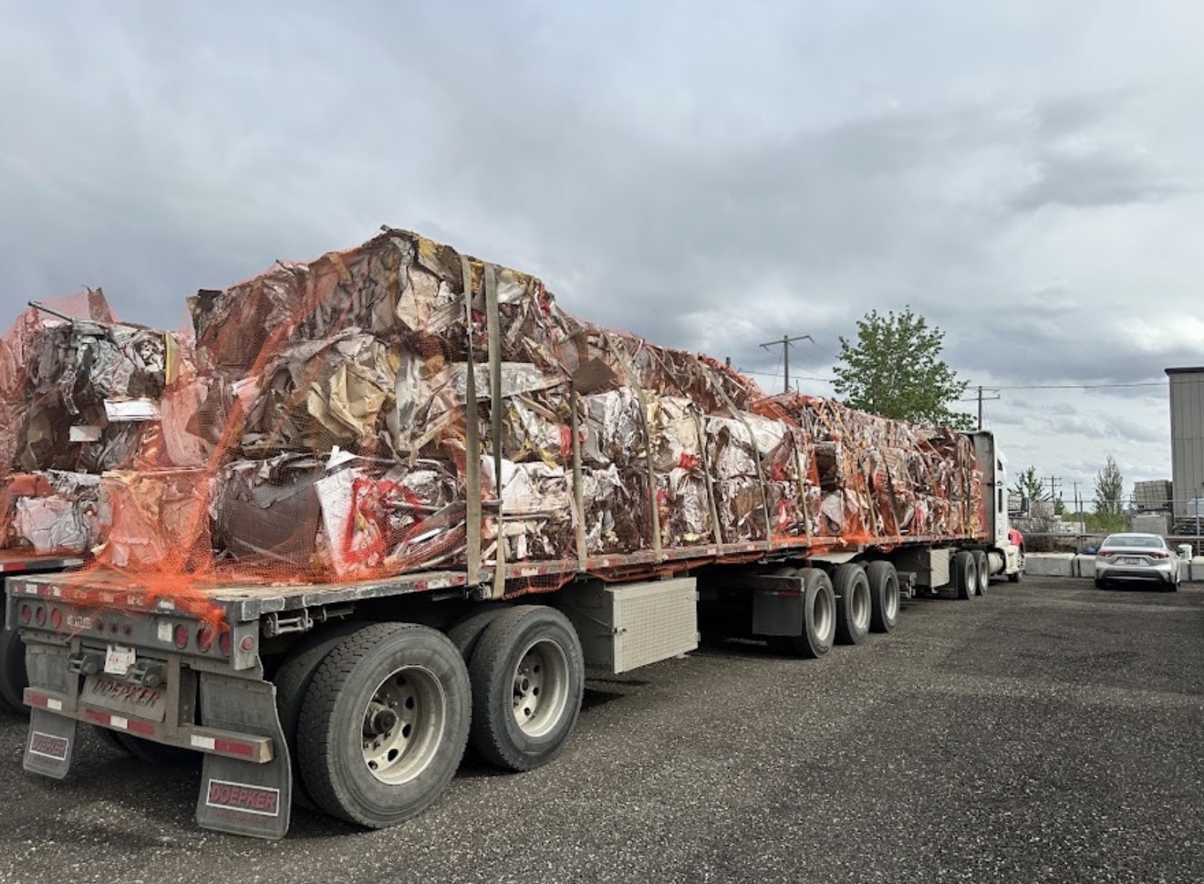 Flatbed loaded with baled scrap metal wrapped in orange safety netting