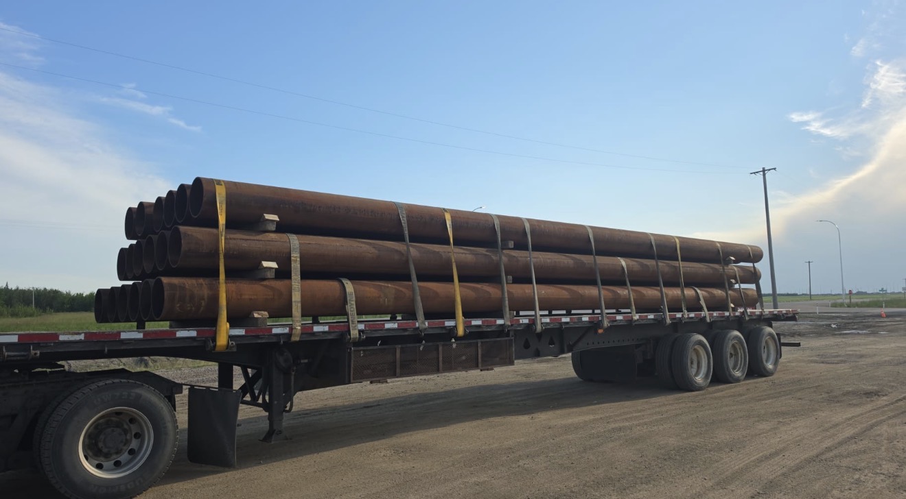 Steel pipe secured on flatbed trailer with chains and straps