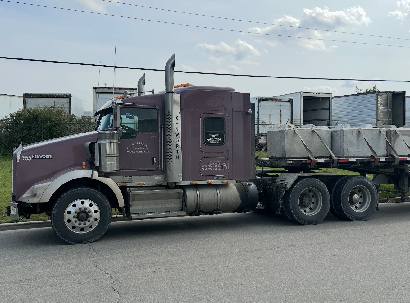 Deep plum Kenworth tractor with flatbed loaded with large concrete barrier blocks